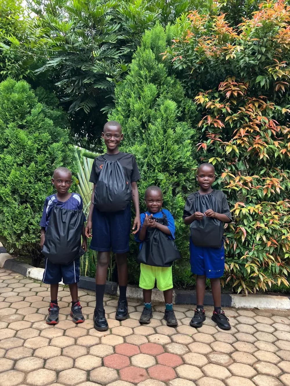 Four children in school uniforms with backpacks, standing in a garden