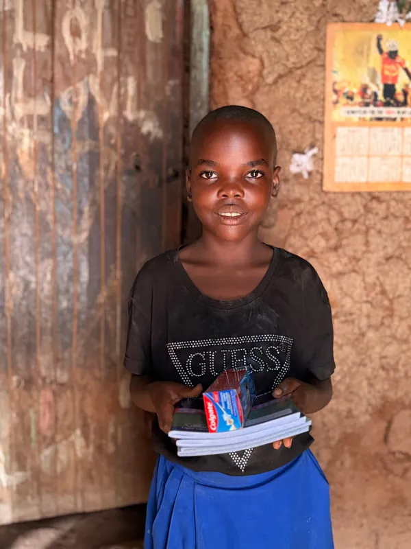 A smiling child holding notebooks and pens